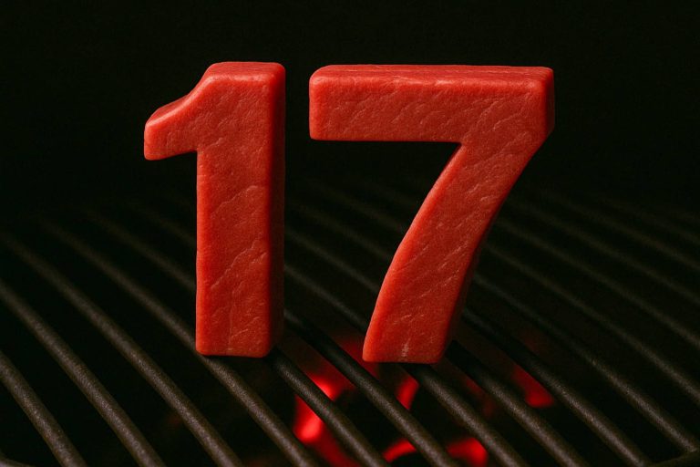 המספר 17 מעוצב מבשר אדום נא ומוצב זקוף על גריל שחור עם גחלים זוהרות מתחתיו, על רקע כהה.