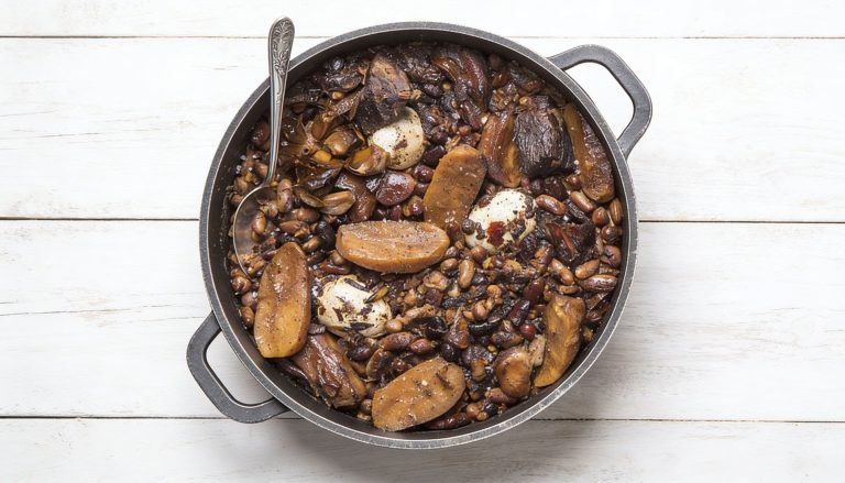 סיר עגול מלא בתבשיל מסורתי שבושל לאט, הכולל שעועית, תפוחי אדמה, ביצים ובשר, מונח על משטח עץ לבן, וכף הגשה מונחת בתוך הסיר.